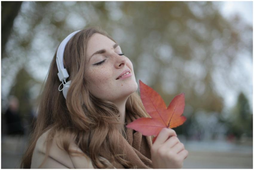 Young woman with headphones holding a red leaf, en