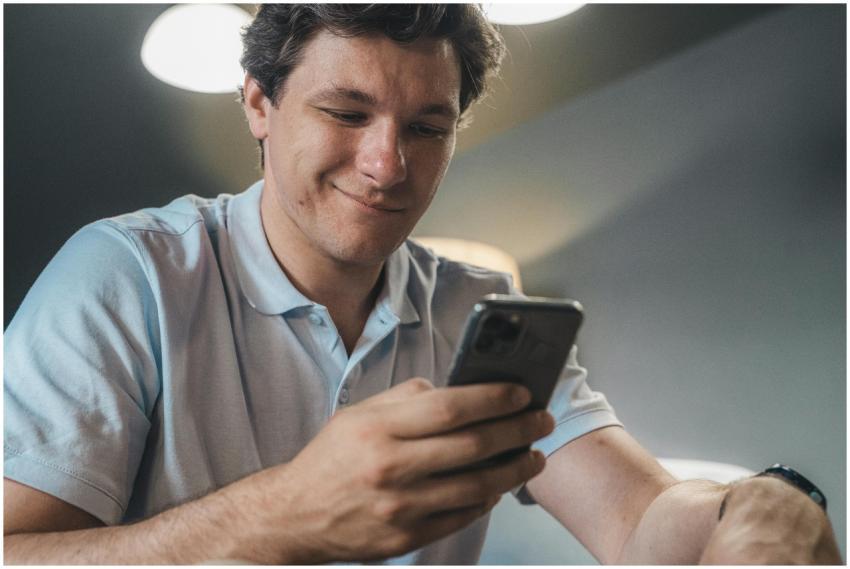 A man in a blue polo shirt smiling while using a s