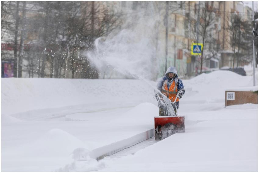 Person using a snow blower to clear a city sidewal