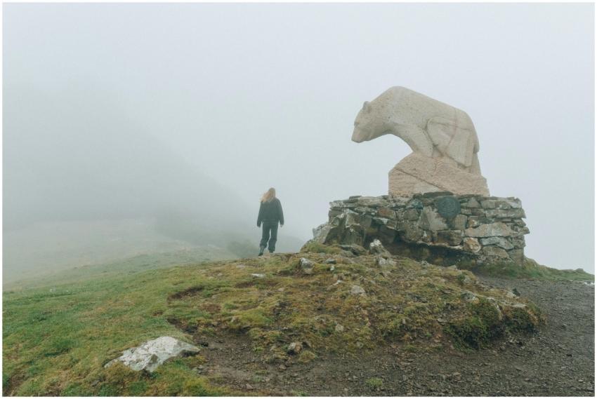 A person hikes toward a bear statue on a misty mou