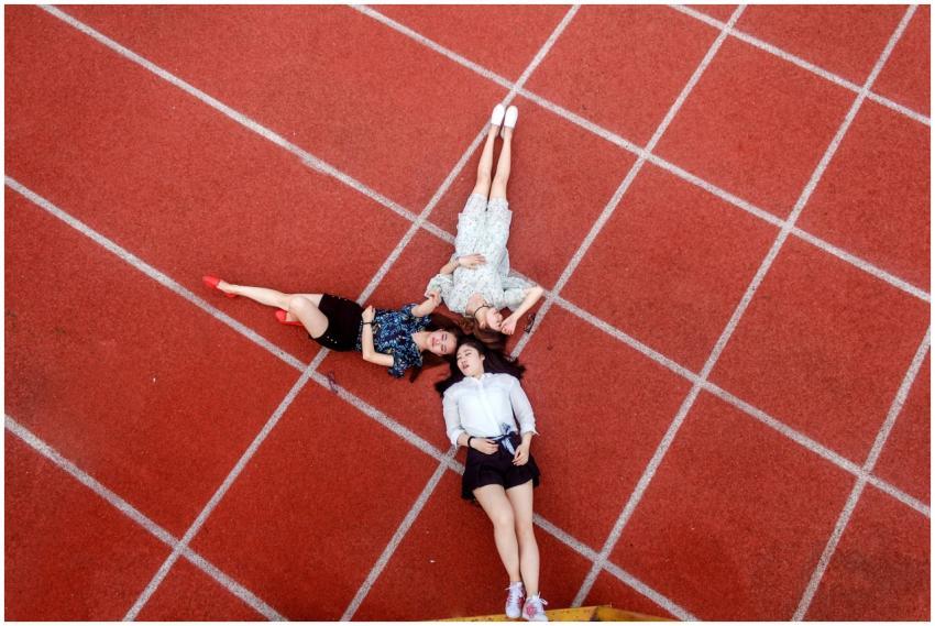 Three young women lying on a red running track, vi