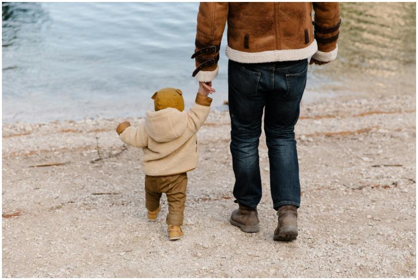 A father and child walk hand-in-hand along a calm