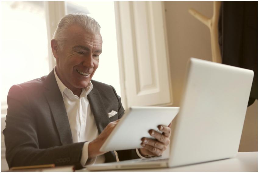 Smiling senior man multitasking with a laptop and