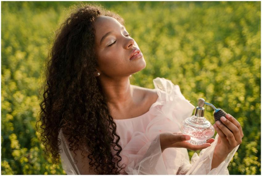 A woman with curly hair holds perfume in a sunlit