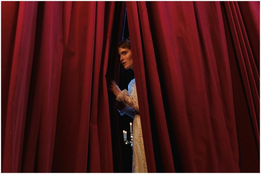 Woman peeks through red theater curtains, capturin