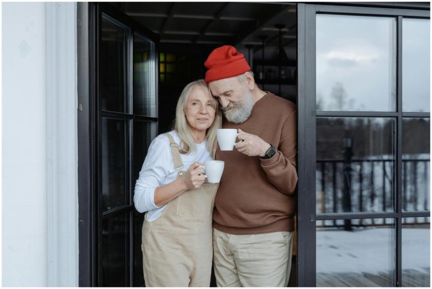 Happy senior couple stands with coffee by the door