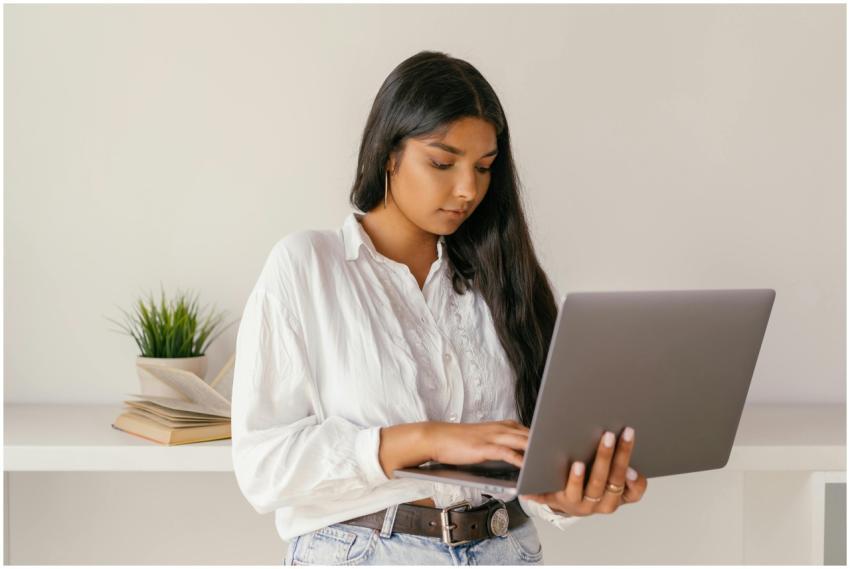 A young woman typing on a laptop while standing in
