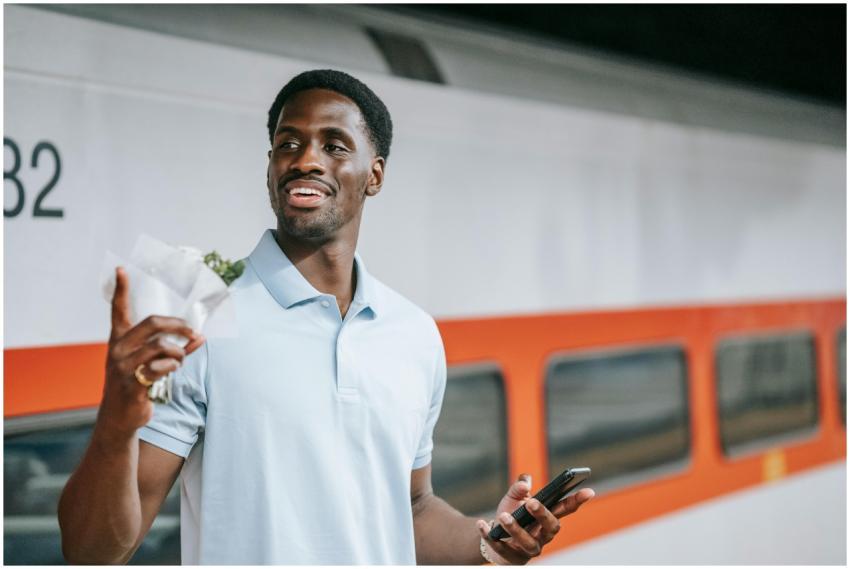 A man stands at a train station holding a smartpho