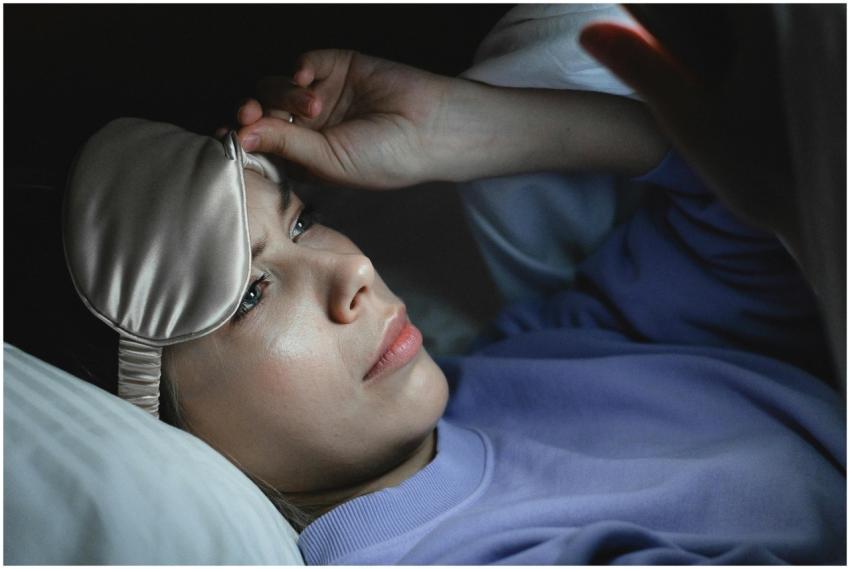 A woman in bed peeking under a sleep mask to use h