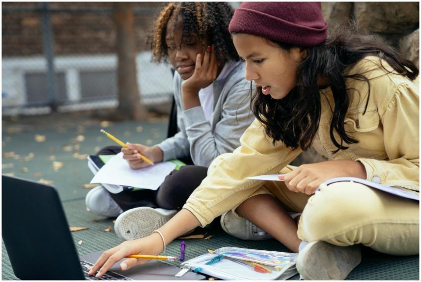 Two teenage girls studying together outdoors, focu