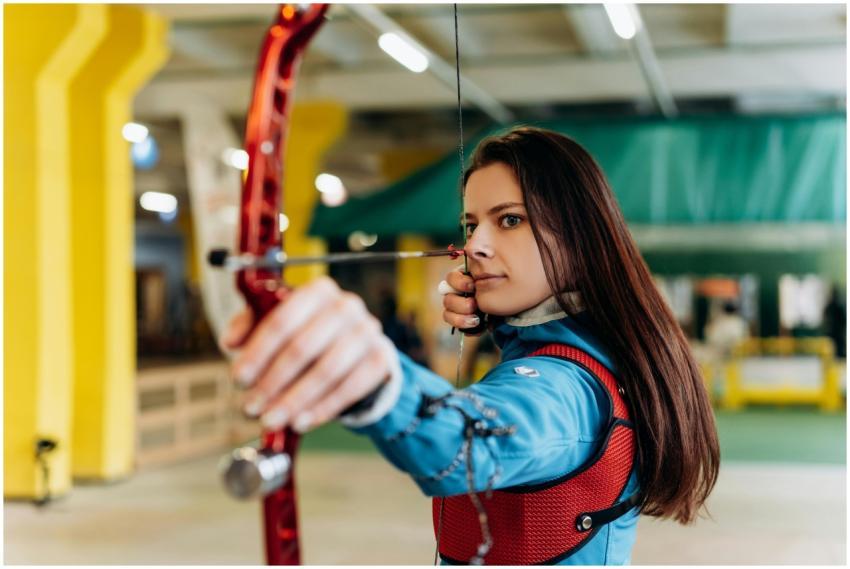 Young woman practicing archery indoors, showcasing