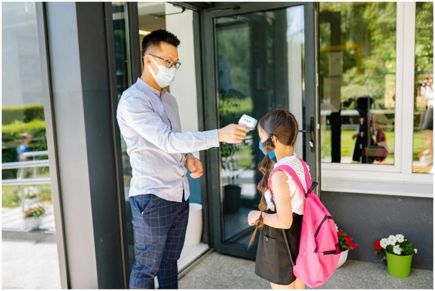 A teacher checks a student's temperature as she ar