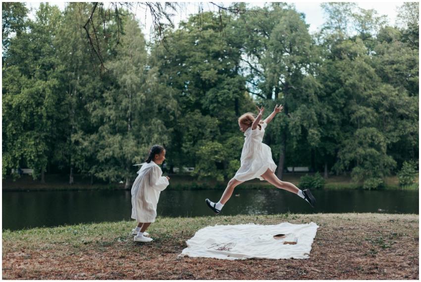 Two girls in white dresses playing joyfully by a l