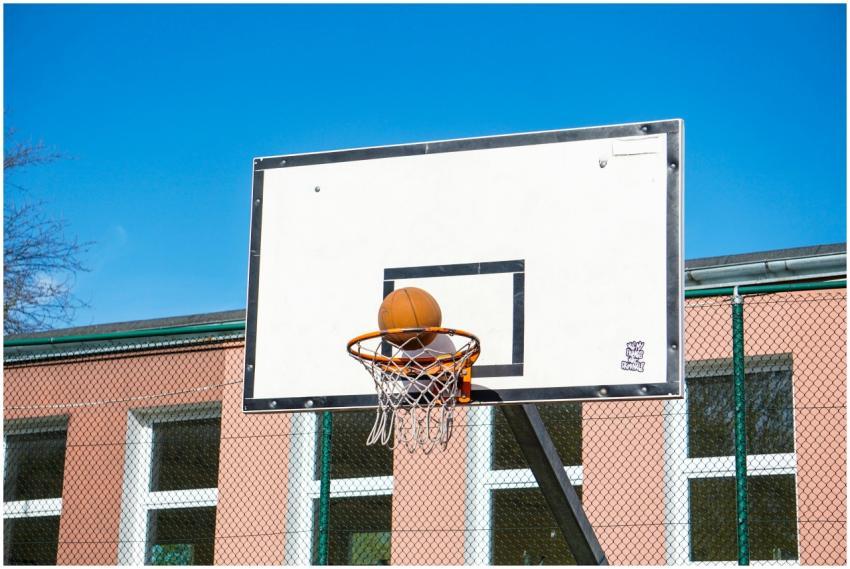 A basketball sits in a hoop against a clear blue s