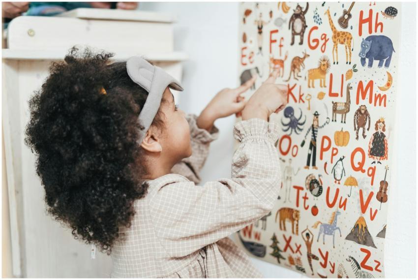 Child with curly hair points to an animal alphabet