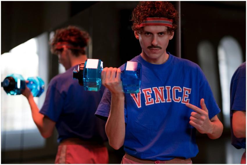 Young man lifts a blue dumbbell indoors, reflected