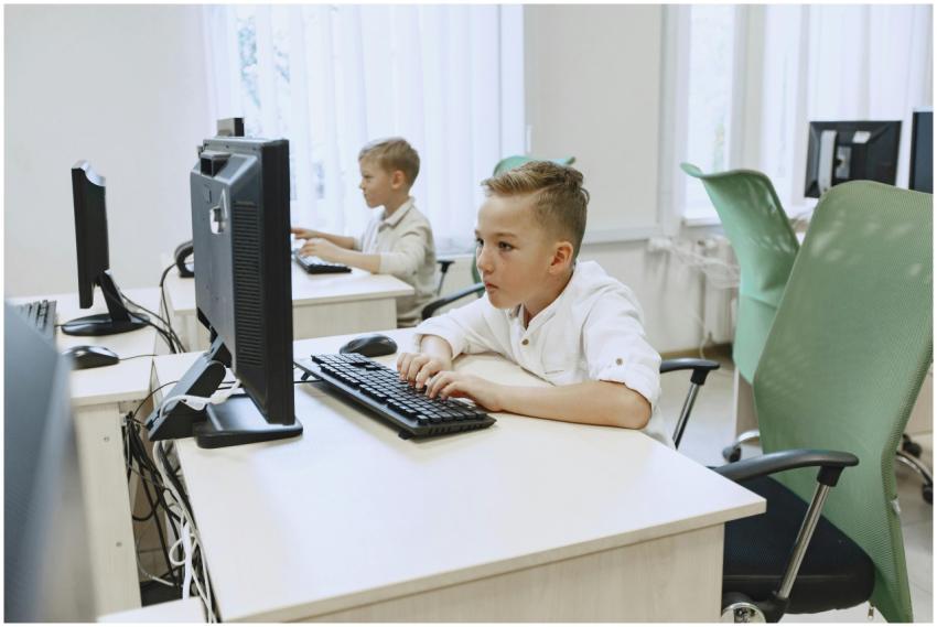 Two young boys focused on computers in a bright, m