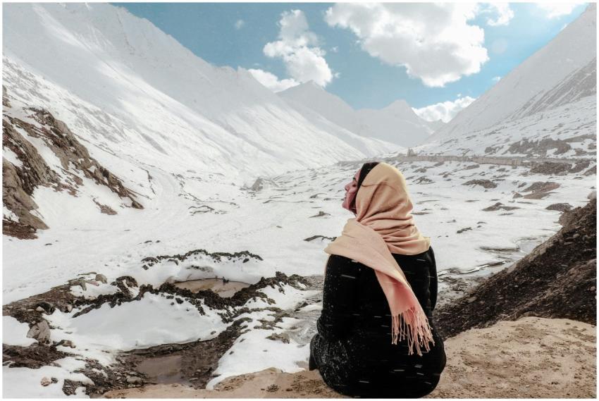 A woman sits on a snowy mountain, wrapped in a sca