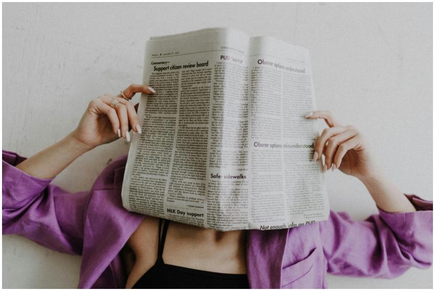 A woman in a violet jacket holds a newspaper, obsc