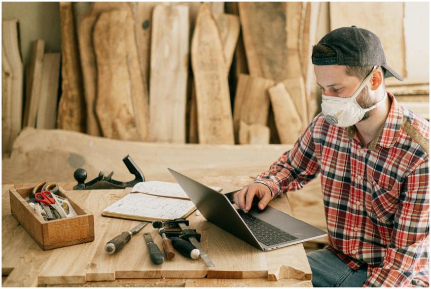 A craftsman wearing a mask, working on a laptop in