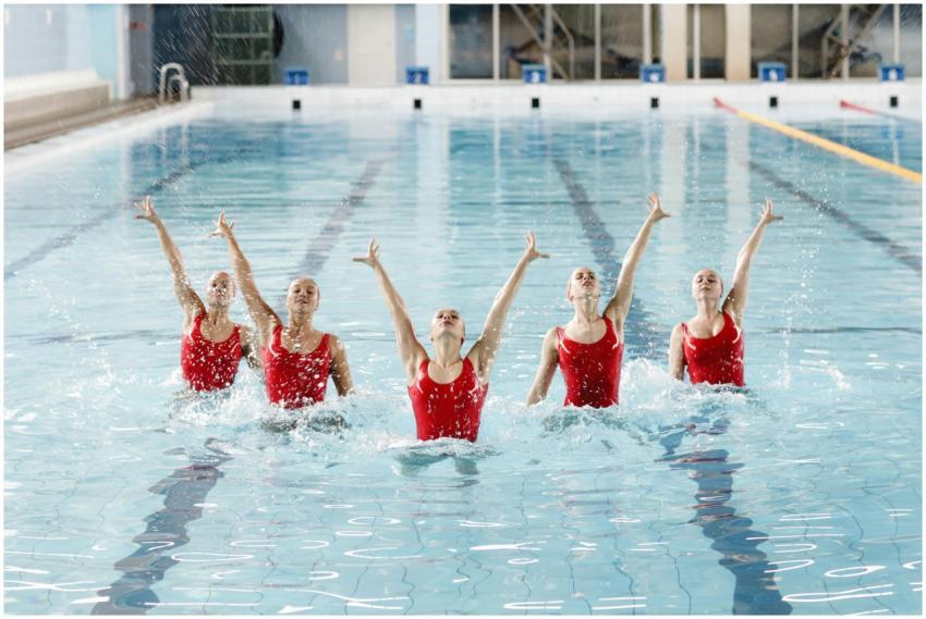 Synchronized swimmers in red suits performing in a
