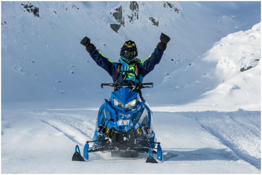 Snowmobiler raising arms in triumph on a snowy mou