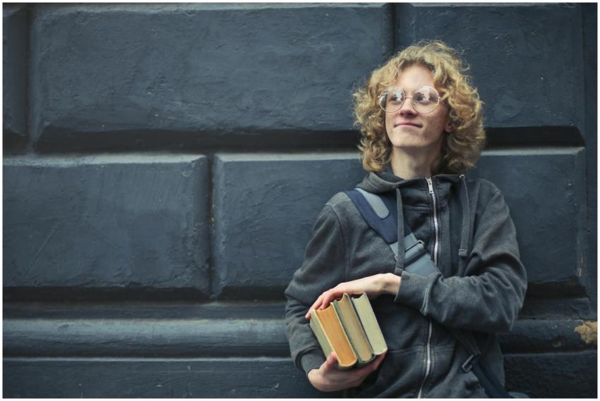 A smiling young man with glasses and messy hair ho