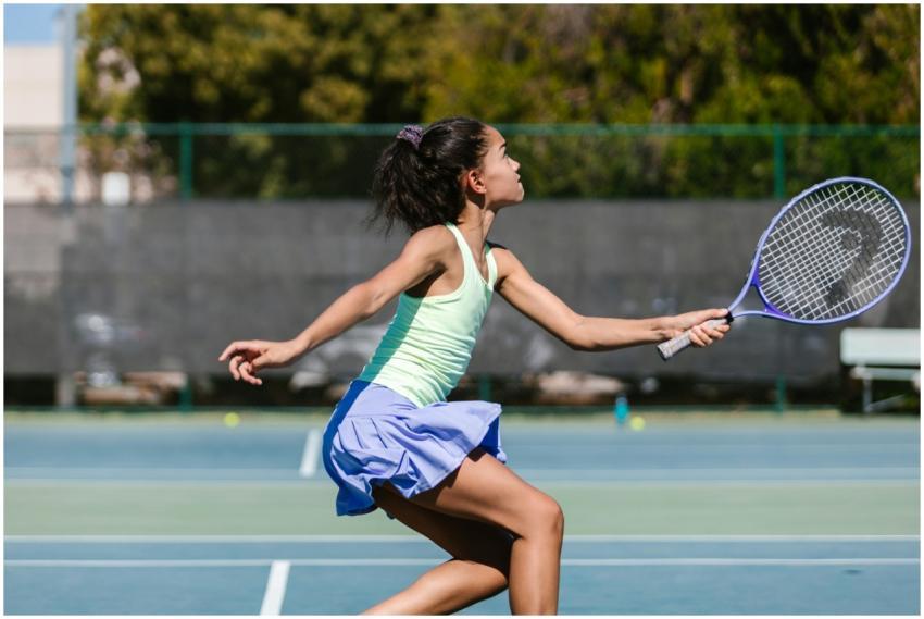 A young girl energetically hits a tennis ball on a