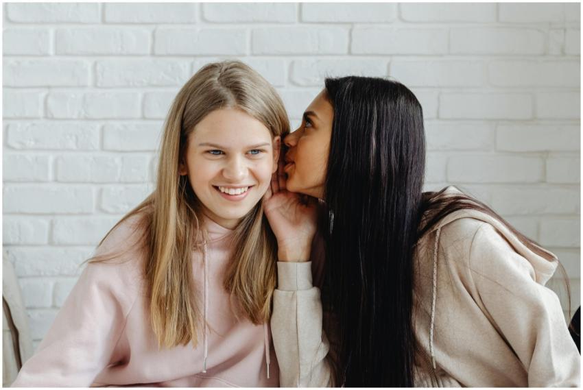 Two teenage girls whispering indoors, sharing secr