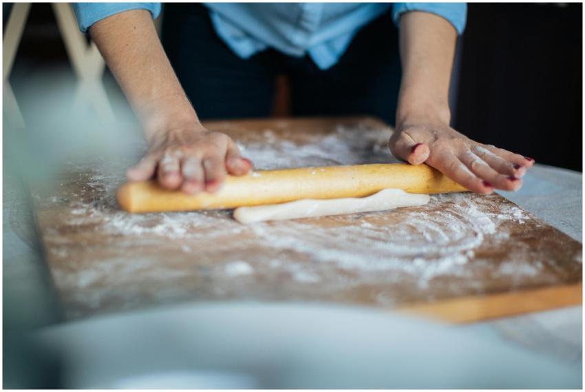 Hands rolling dough with a wooden rolling pin on a