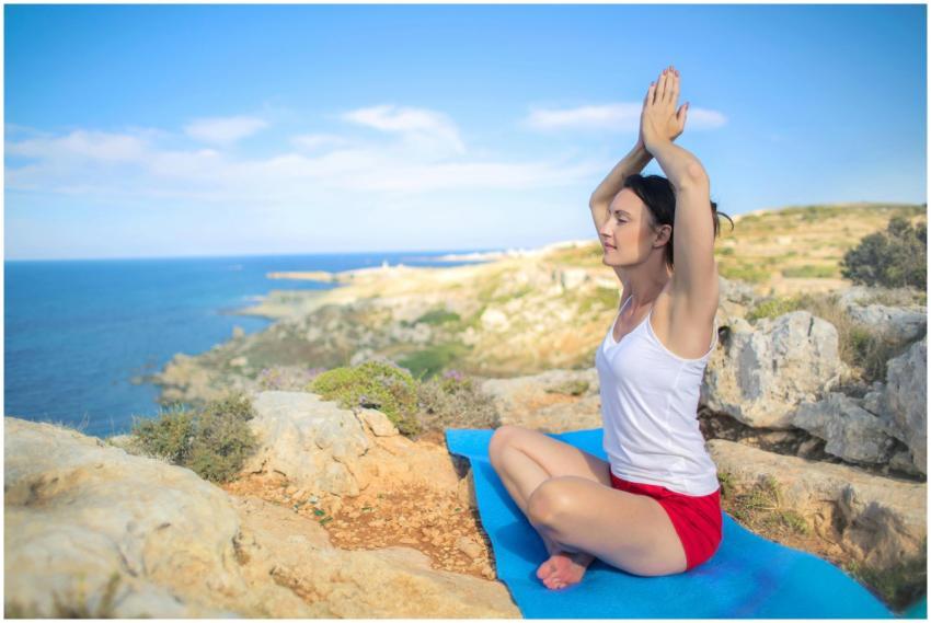 A woman practicing yoga on a rocky seaside with cl
