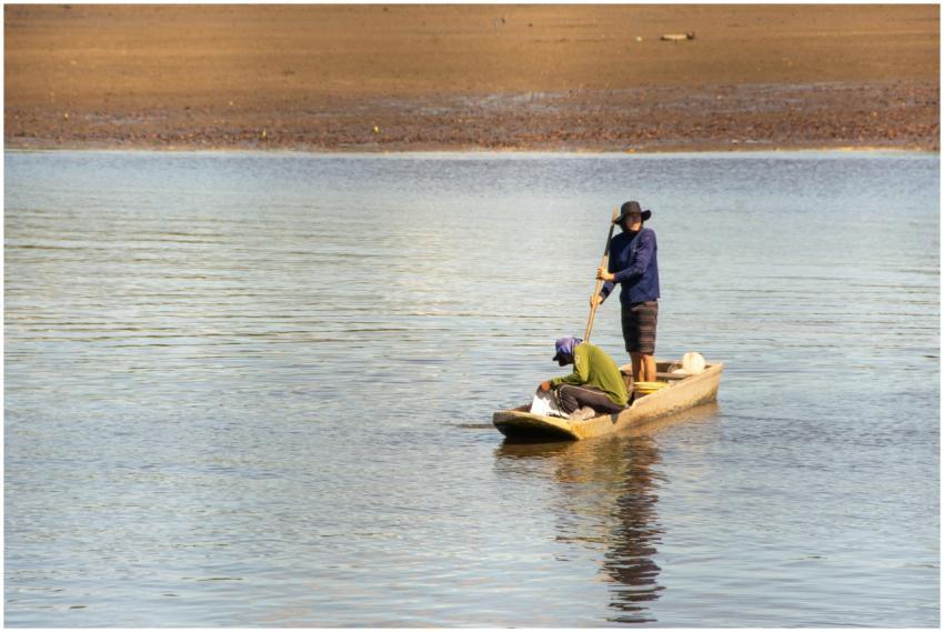 Two fishermen navigate a small canoe on tranquil w