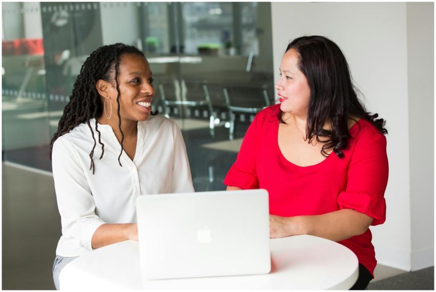 Two women in an office discussing work using a lap