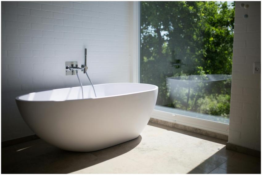 Sleek white bathtub by large window in sunlit mini