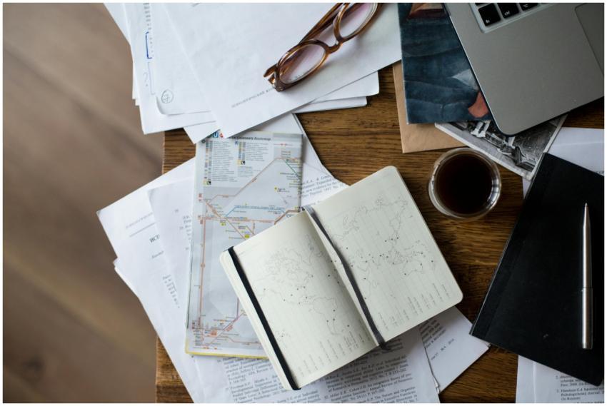 Flat lay of a workspace with coffee, maps, laptop,