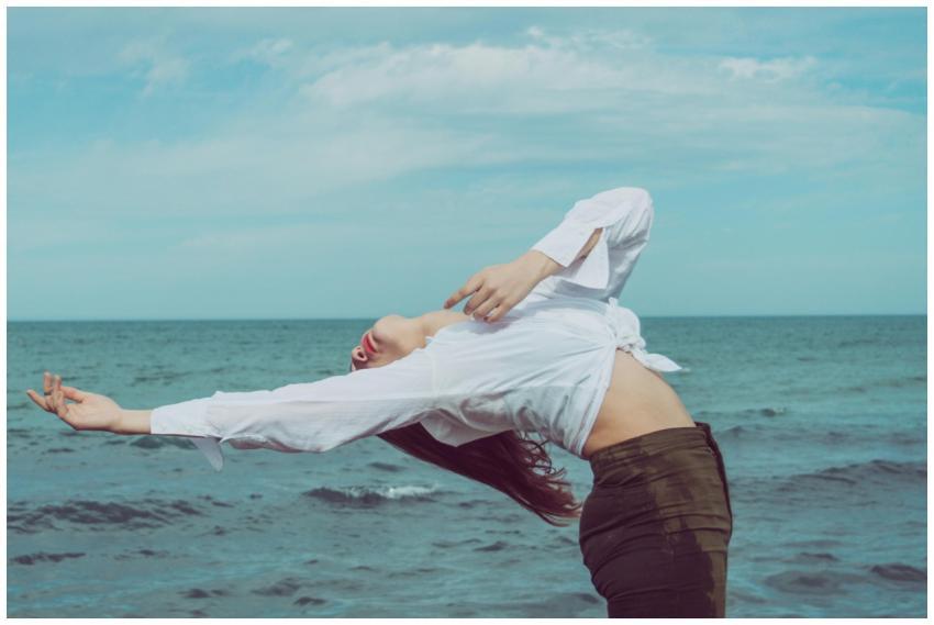 A woman performing a yoga pose by the ocean, captu