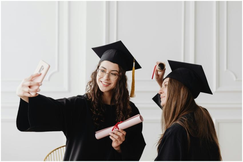 Two happy female graduates in academic gowns takin