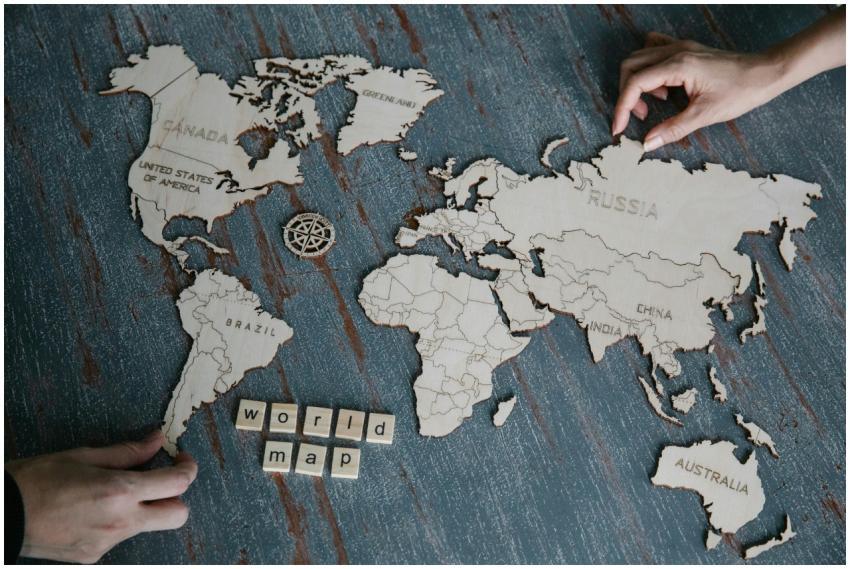 Hands assembling a wooden world map puzzle on a da