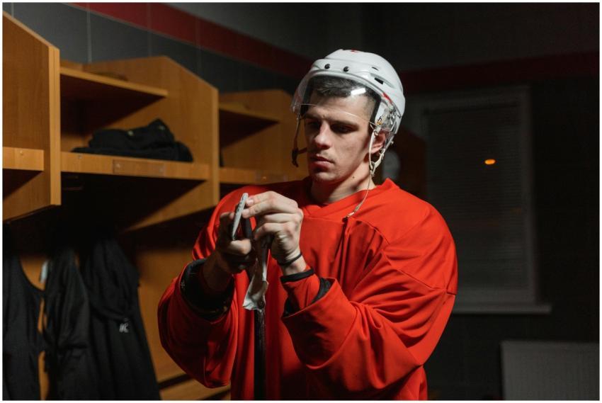 Male hockey player in locker room preparing stick,