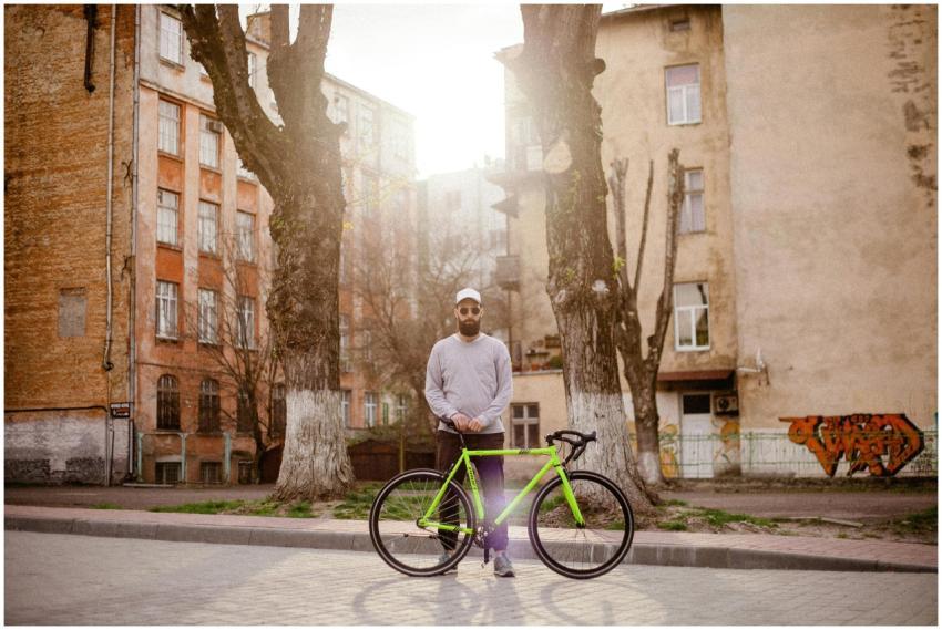 A man stands with a green bicycle on a sunlit stre