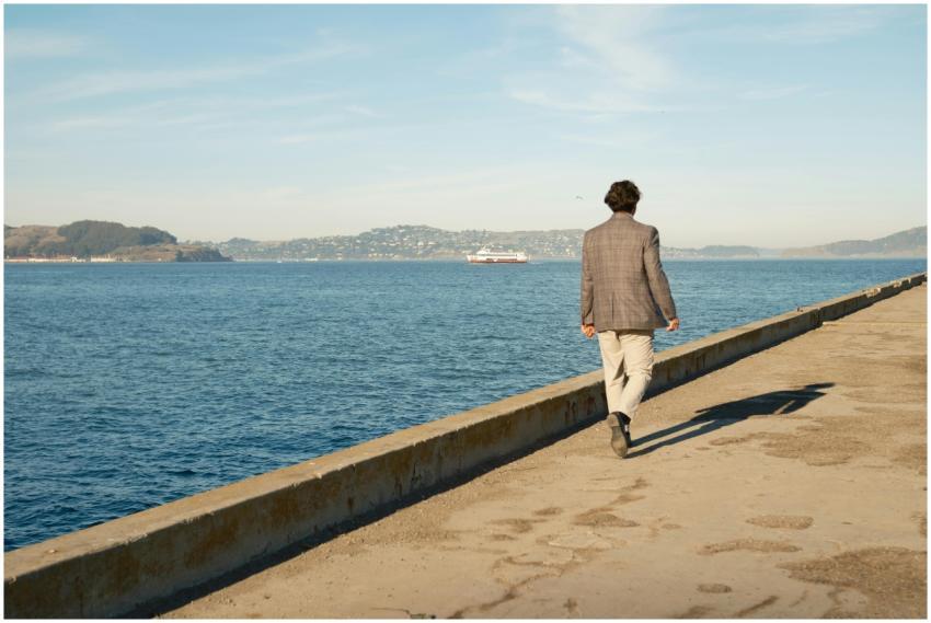 A man in a suit walks along a pier by the ocean in