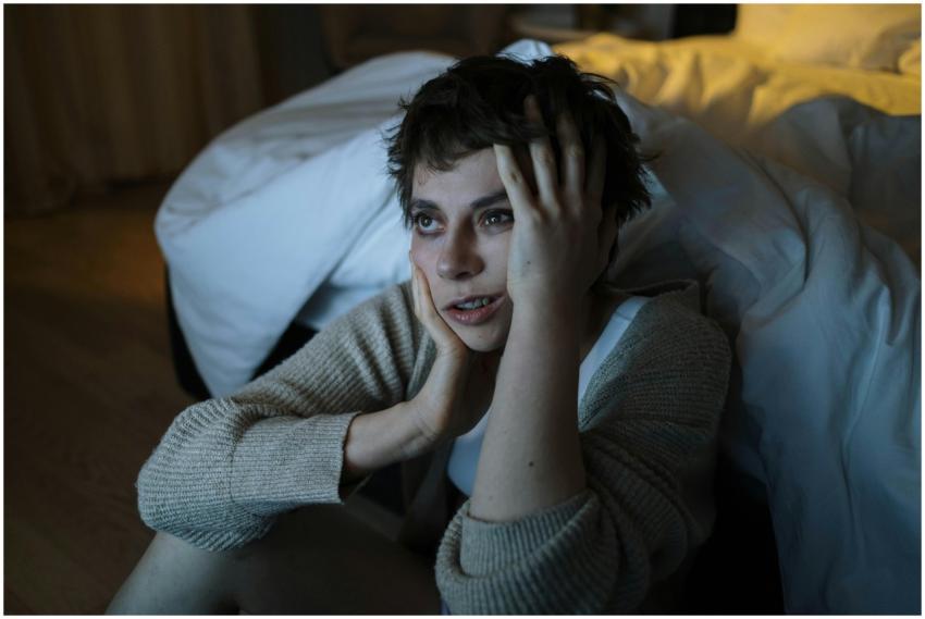 A woman sitting on the floor by a bed with a worri