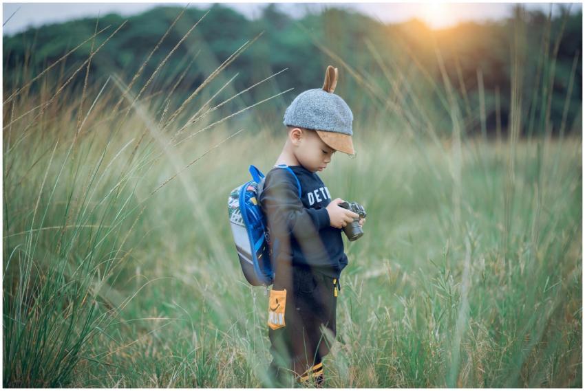 A young boy wearing a cap explores a grassy field