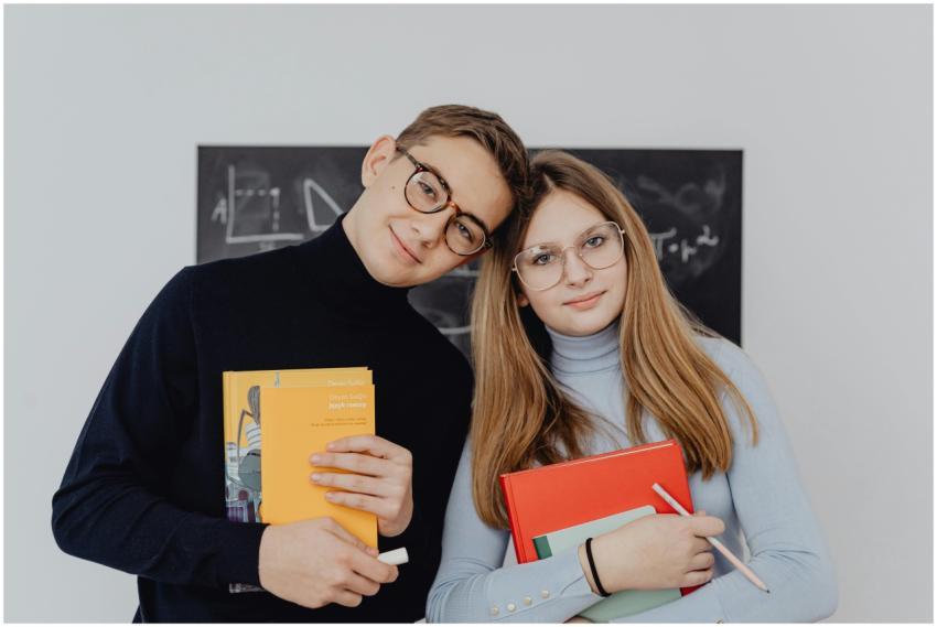 Two students holding books against a blackboard, s
