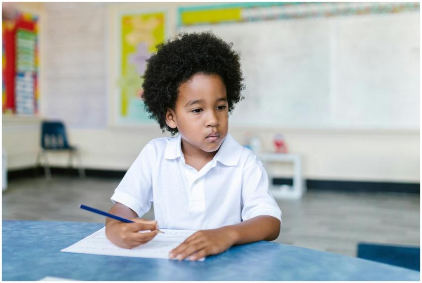 A focused young boy with afro hair writing in a cl