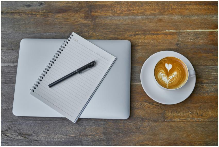 Flat lay of a coffee cup, notebook, pen, and lapto