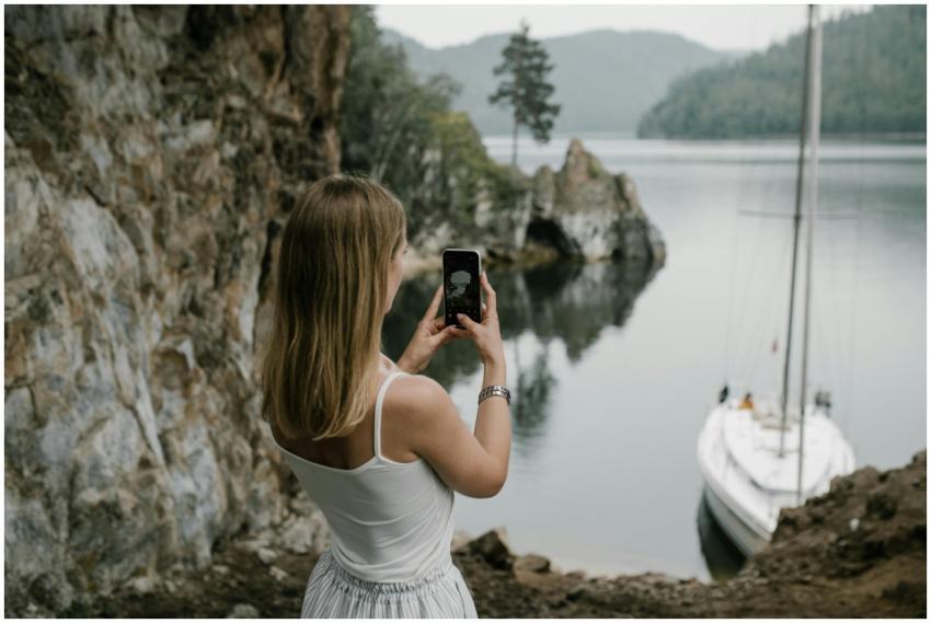 A woman takes a photo of a serene lakeside with a