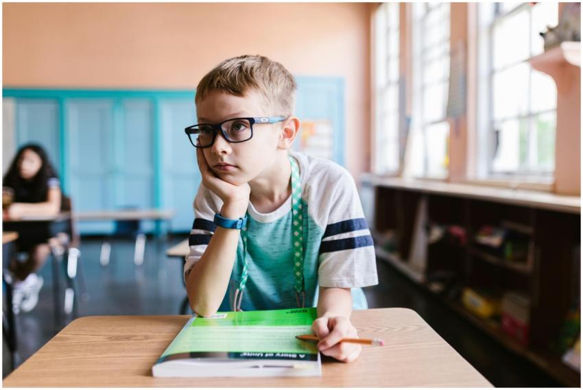 A young boy wearing eyeglasses sits at a desk in a