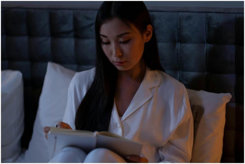 Asian woman in pajamas reading notebook in bed, cr