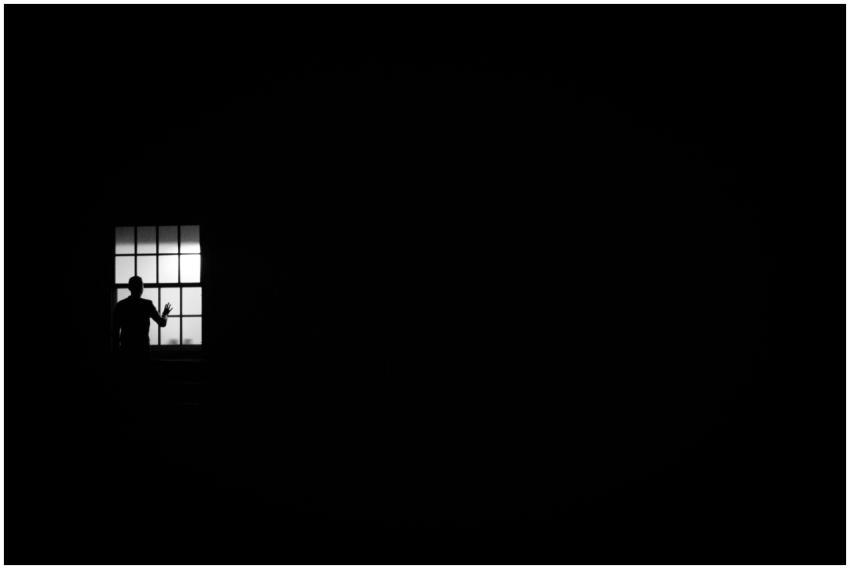 A solitary silhouette at a window against a black